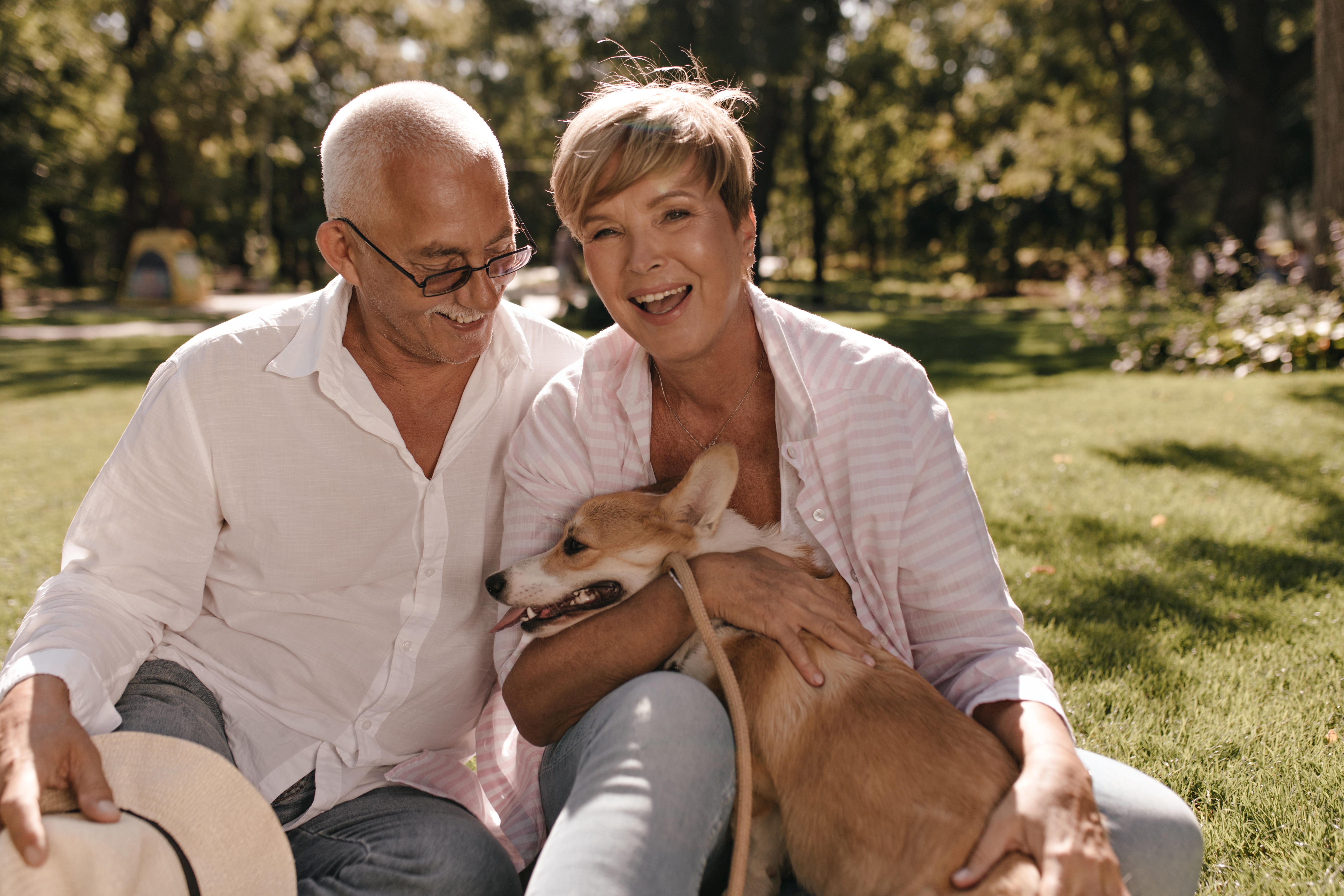 cheerful-lady-with-short-blonde-hair-pink-shirt-laughing-hugging-dog-sitting-grass-with-grey-haired-man-eyeglasses-park.jpg